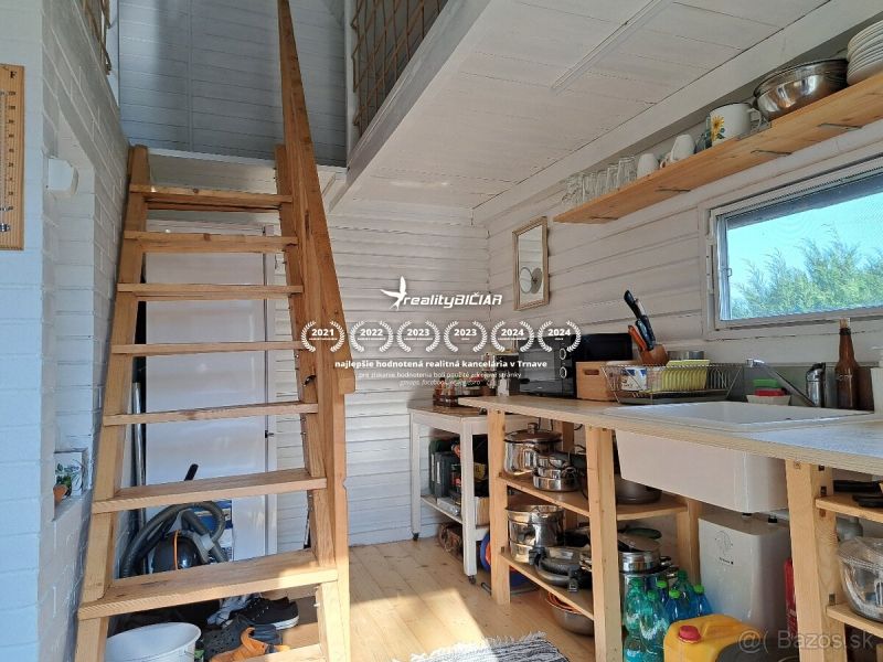 Interior of a cabin with a staircase, kitchen, and wooden decor flooring.