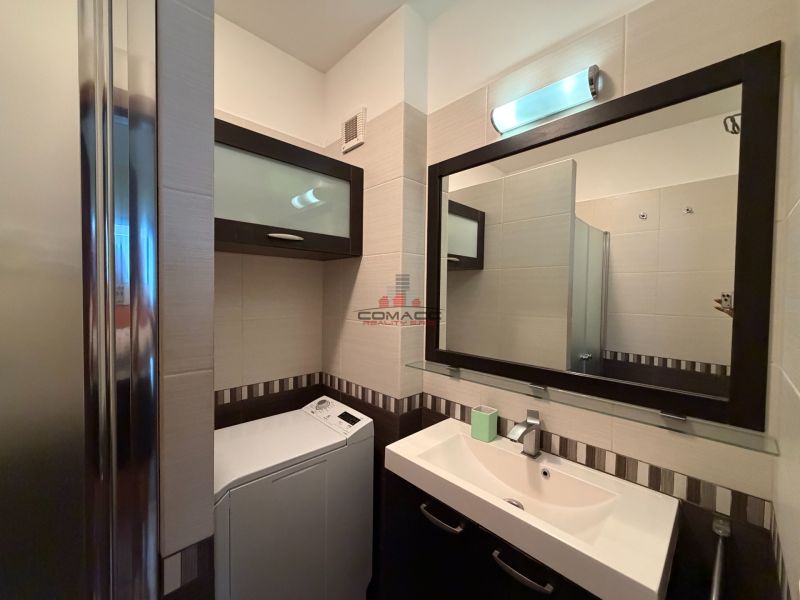 A bathroom with a sink, mirror, shower, and washing machine in a 3-room apartment.