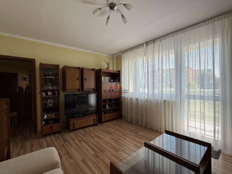 Living room in a three-room apartment with a wooden decor floor and large windows.