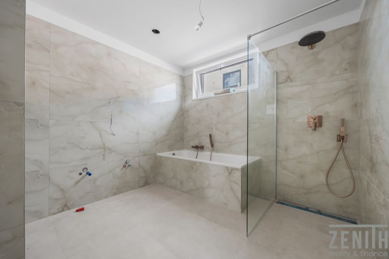 A bathroom in a family house with a bathtub and a shower, tiled with light tiles.