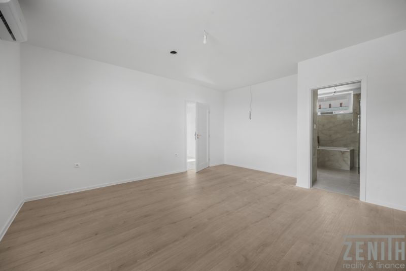 A nondescript room in a family house with a wood-patterned floor and white walls.