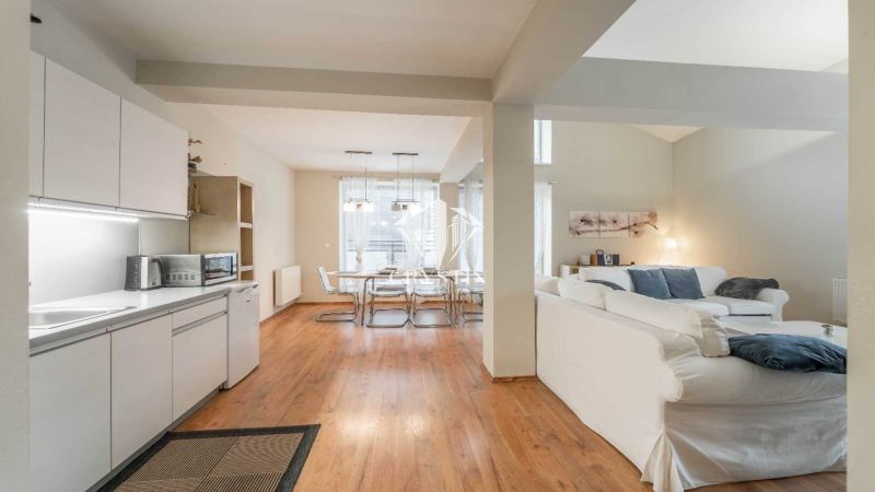A recreational apartment with a wooden decor floor, kitchen, dining table, and comfortable seating.