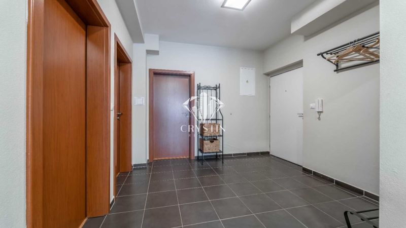 Entrance hall of a holiday apartment with dark tiles, wooden doors, and a coat rack.