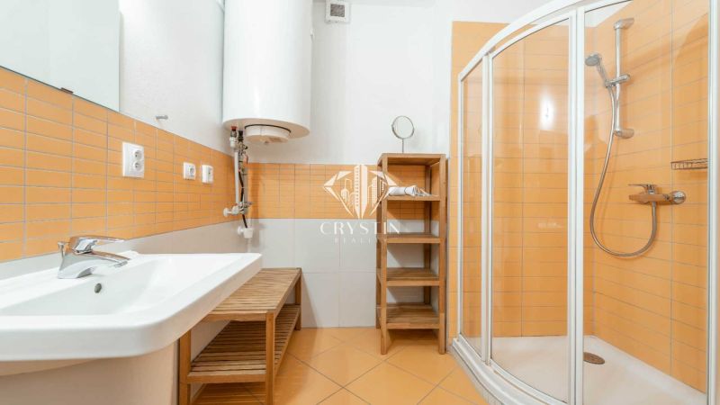A bathroom with orange tiles, a shower corner, and a sink in a holiday apartment.