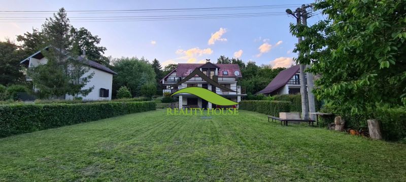 A cottage in Kaluža surrounded by greenery, maintained lawn, surroundings with trees, blue sky.