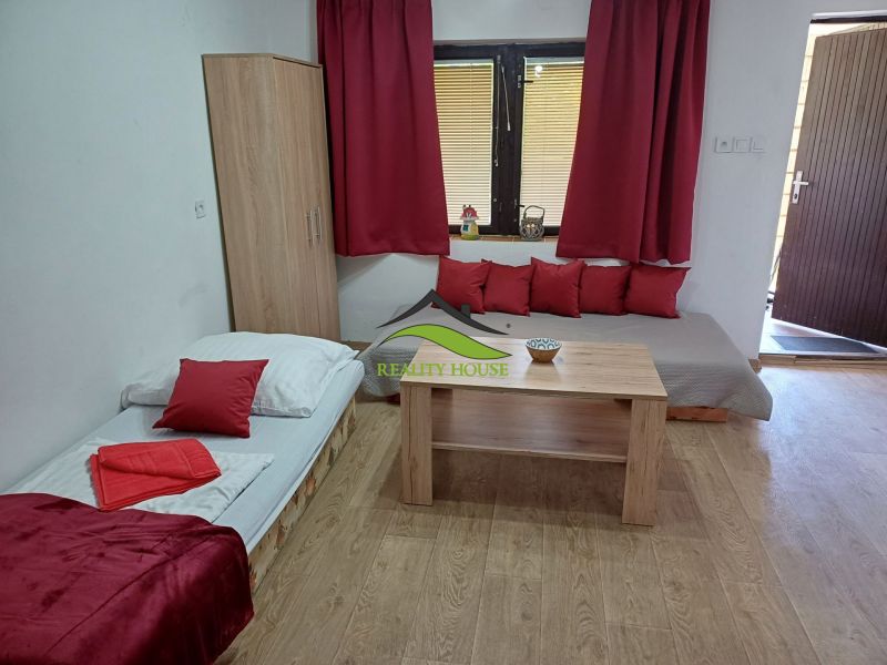 Interior photograph of a cabin with a bed, table, and red accessories.