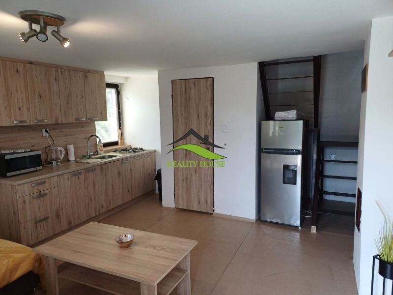 Interior of a cabin with a kitchen unit, refrigerator, and staircase, floor with wooden decor.