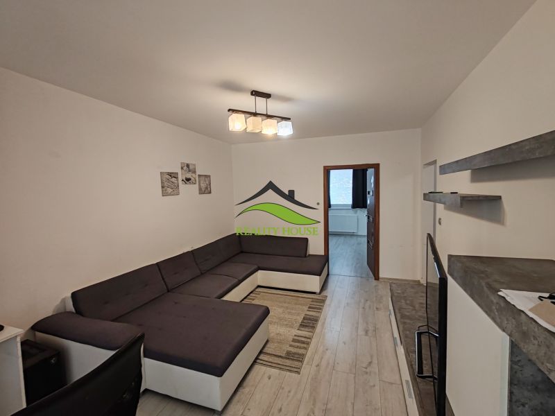 Living room with a large sofa, wooden decor flooring, and simple interior in a 3-room apartment.