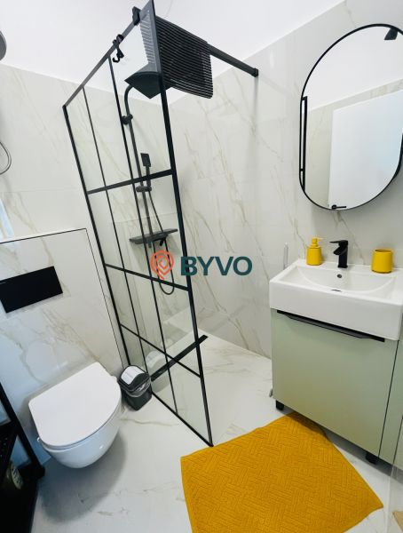 A bathroom in a 2-room apartment with a shower, a wall-hung toilet, and an orange rug.