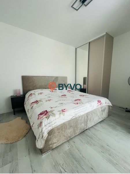 Bedroom in a 2-room apartment with a bed and a wardrobe, light walls, floor with wooden decor.