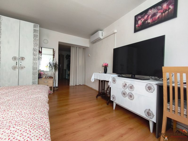 Bedroom with wood-patterned flooring, television, cabinet, and floral decoration.