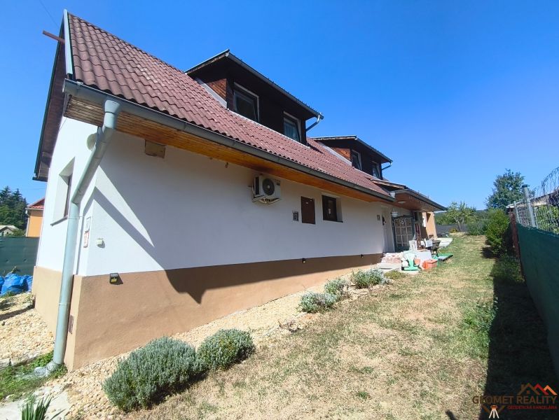 A family house in Divín with a brown roof and a garden, bordered by a lawn and shrubs.