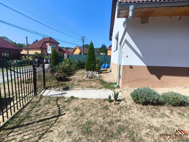A garden at a family house in Divín with plants and a lawn, surrounded by a fence.