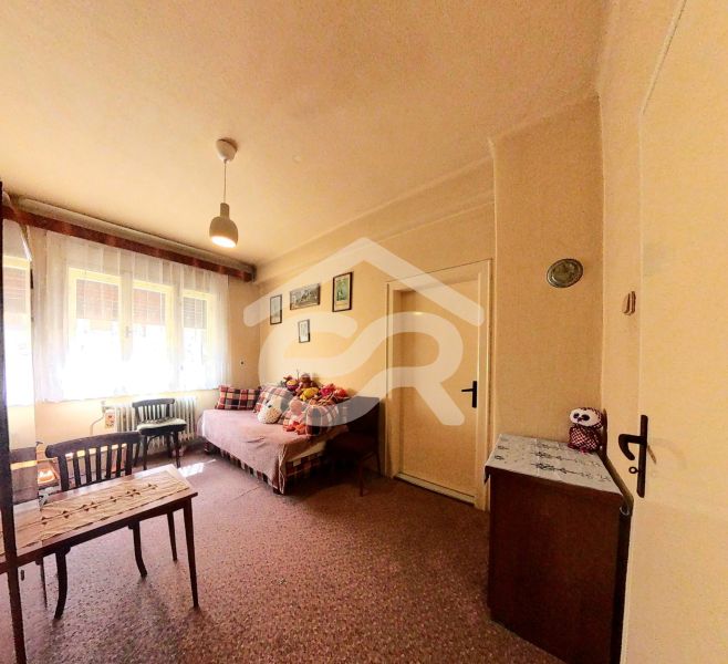A room in a family house with a carpeted floor, a bed, furniture, and toys on the bed.