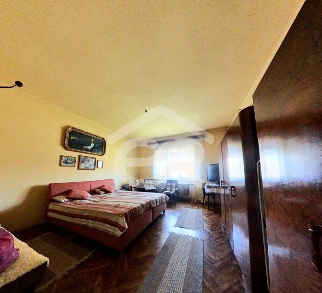 Bedroom in a family house with a wooden decor floor, bed, wardrobes, paintings on the wall.