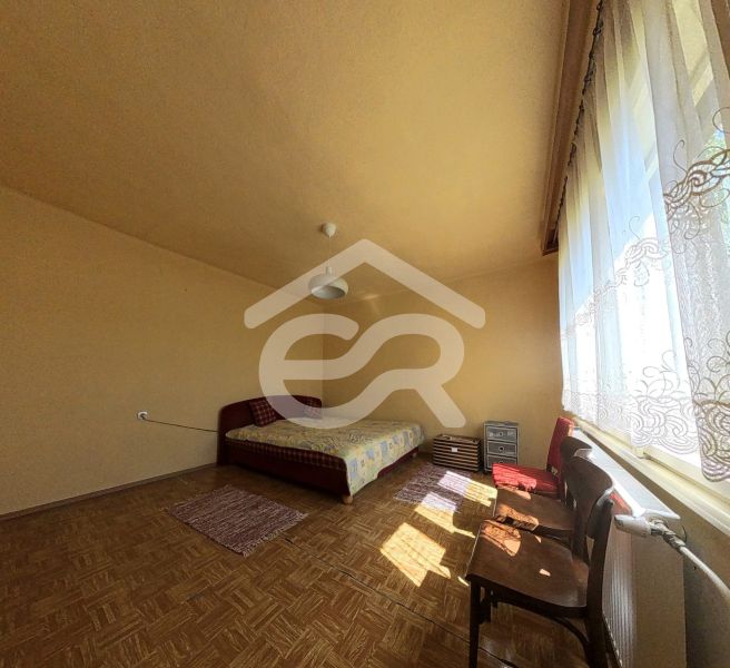 Bright room in a family house with a bed, large window, and wooden decor flooring.