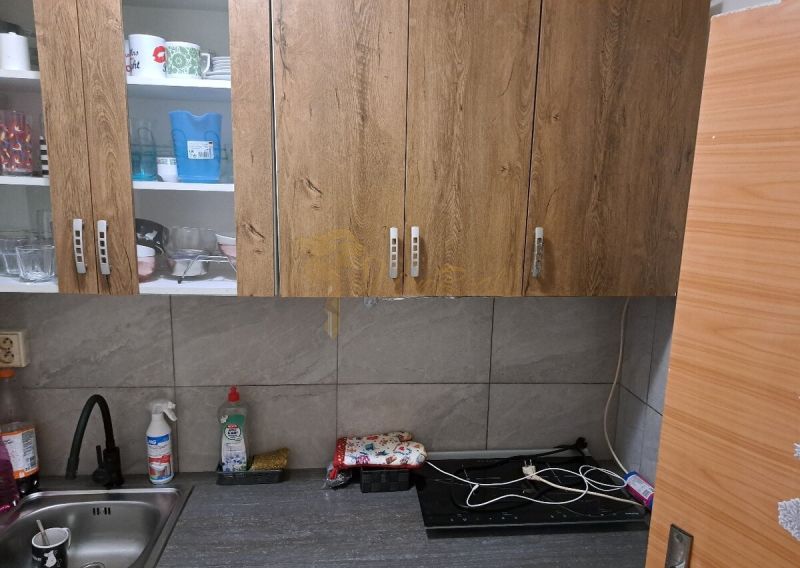 A kitchen with wooden cabinets, a sink, and a countertop in a studio apartment.