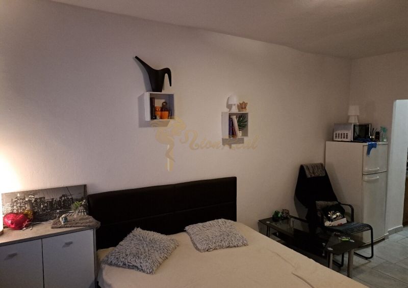 Studio apartment with a bed, wall decorations, and a chair next to the refrigerator.