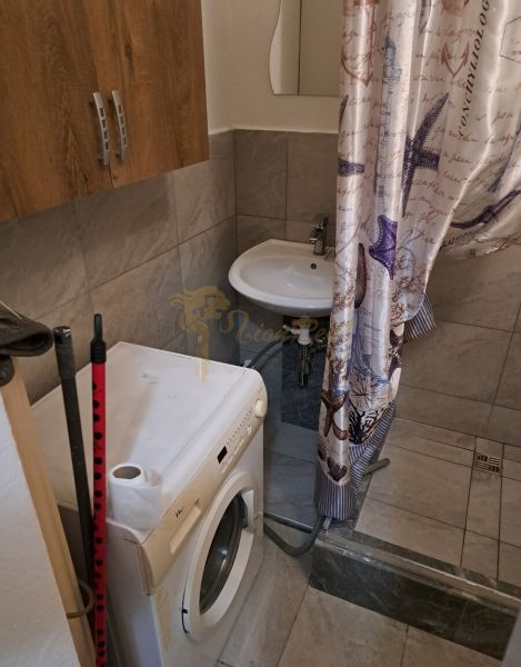 A studio apartment bathroom with a washing machine, shower, and ceramic tiles.