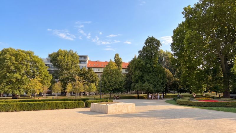 A garden with colorful flowers, trees, and buildings in Bratislava - Old Town on Banskobystrická.