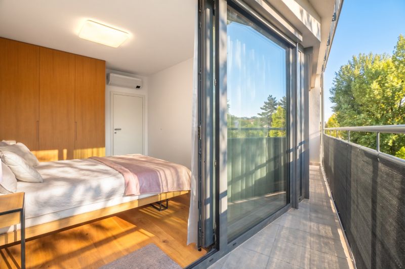 A bedroom with a large glass wall, wood-patterned flooring, and a balcony in a two-room apartment.