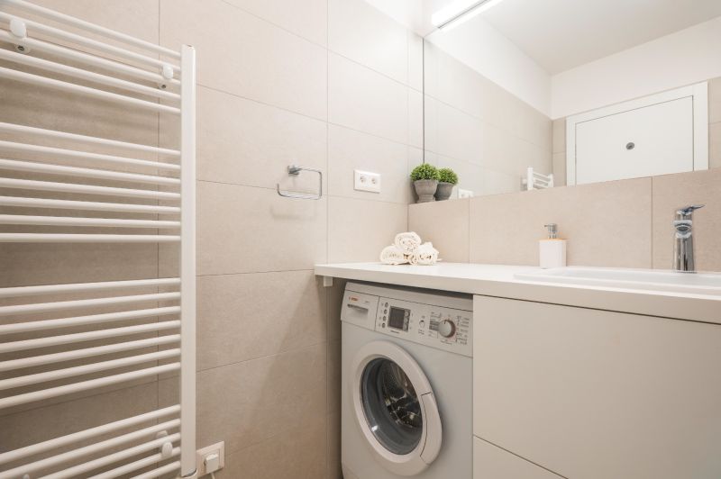 A bathroom with light tiles, a washing machine, a sink, and towels in a 2-room apartment.