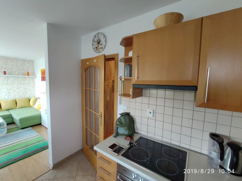 A kitchen in a 2-room apartment with wooden cabinets and a view of the living room.