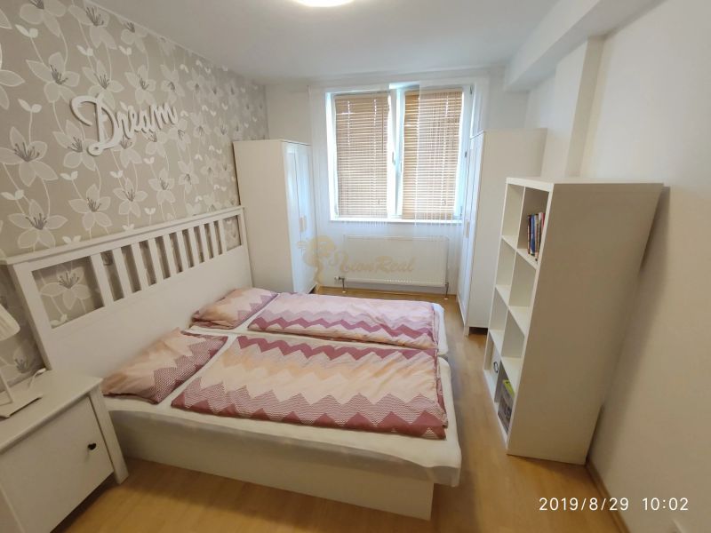 A bedroom with a bed, wooden decor flooring, and floral wallpaper in a two-room apartment.