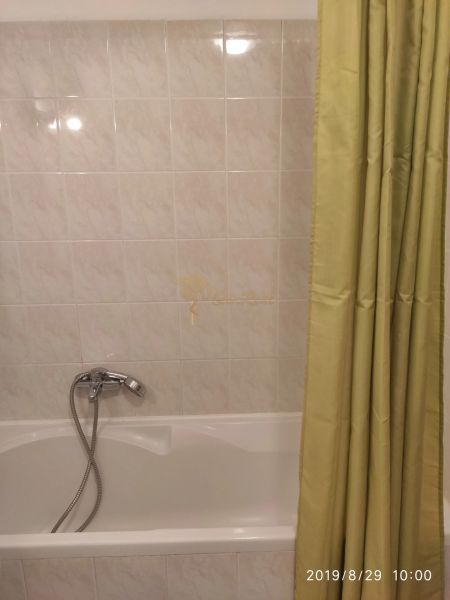Bathroom with white tiles and a bathtub with a curtain in a 2-room apartment.