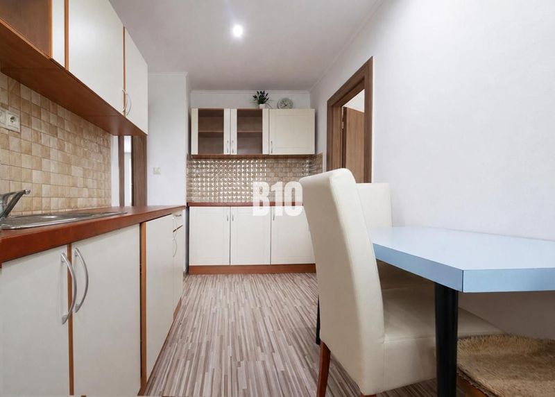 A kitchen in a 3-room apartment with a wooden decor floor and light furniture.