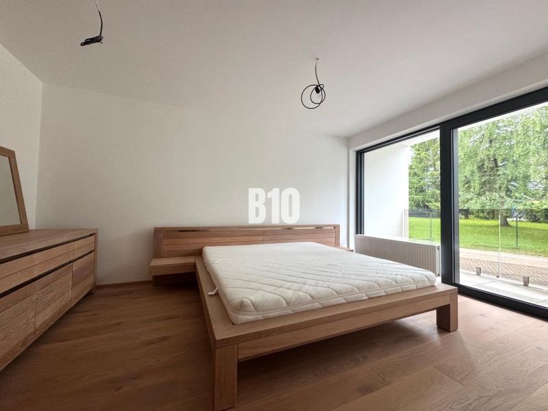 Bedroom with a bed and a dresser, wooden decor flooring, large window facing the garden.