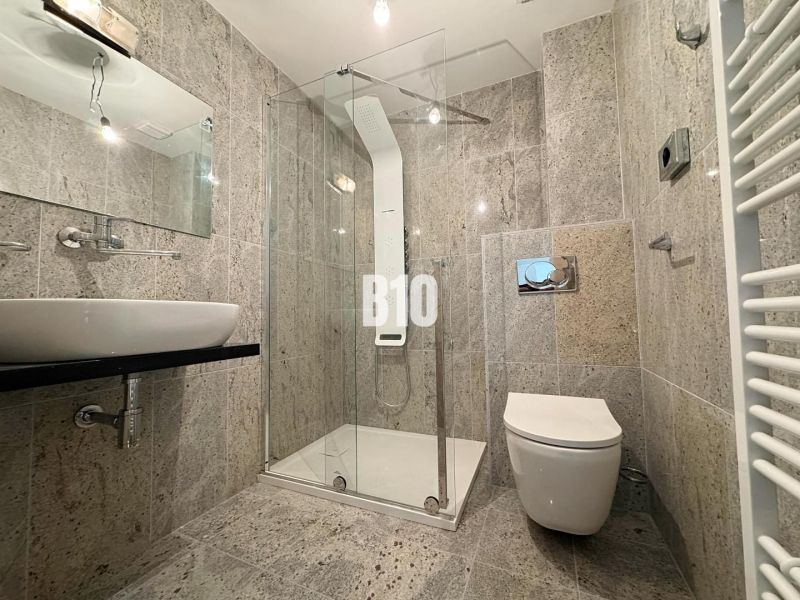 A bathroom in a 2-room apartment with stone cladding, a shower corner, and a mirror.