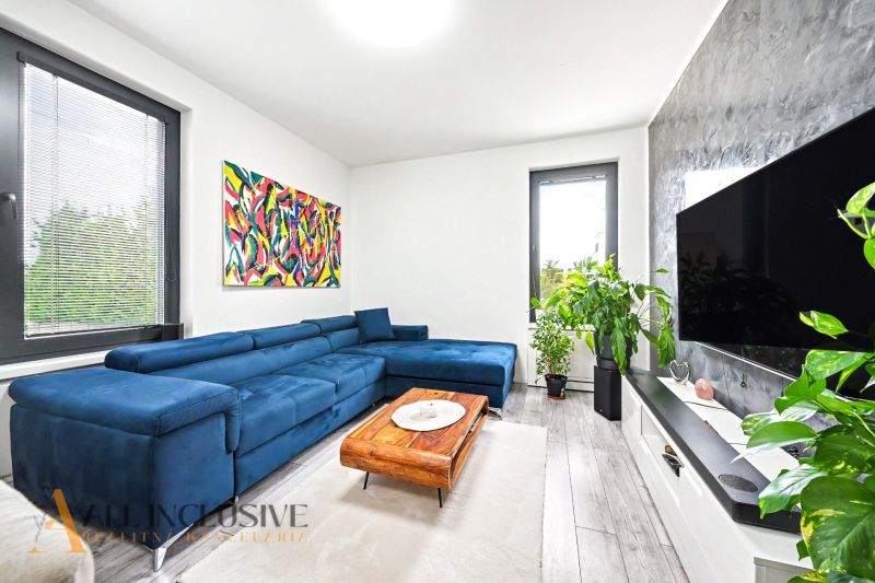 Living room with a blue sofa and plants in a 3-room apartment, floor with wooden decor.