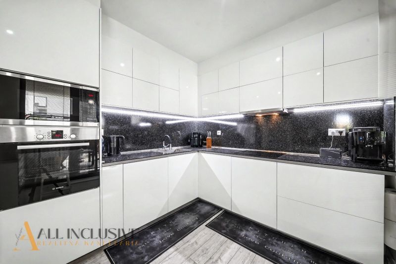 The kitchen of a 3-room apartment with white cabinets and a black countertop.