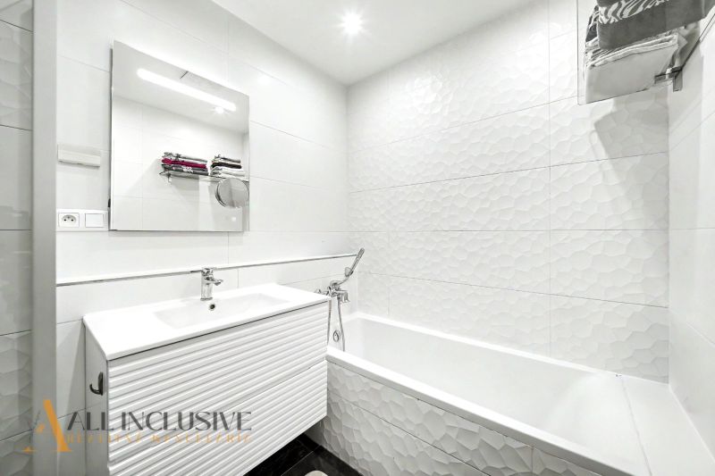 A bathroom with white tiles and a sink in a 3-room apartment.