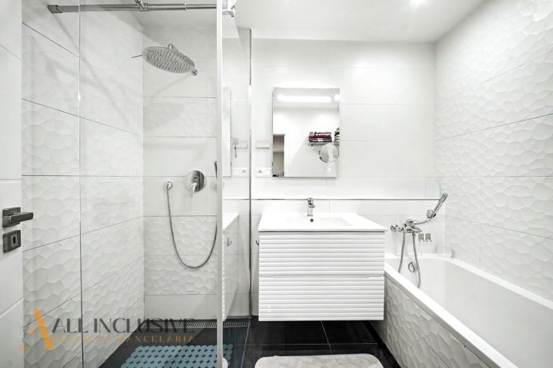 A bathroom with a modern shower and bathtub in a 3-room apartment with white tiles.