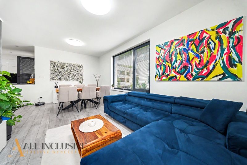 Living room of a three-room apartment with colorful paintings, a blue sofa, and a dining table.