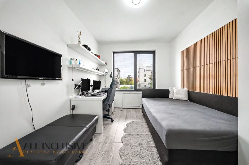 A room in a 3-room apartment with a desk, a sofa, and a wooden decor floor.