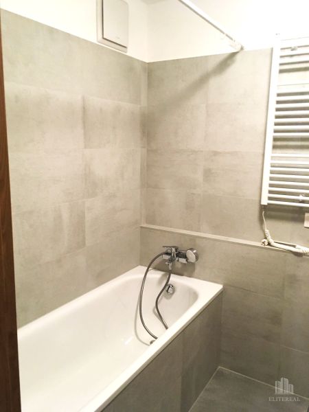 A bathroom with a bathtub and light tiles in a 2-room apartment.