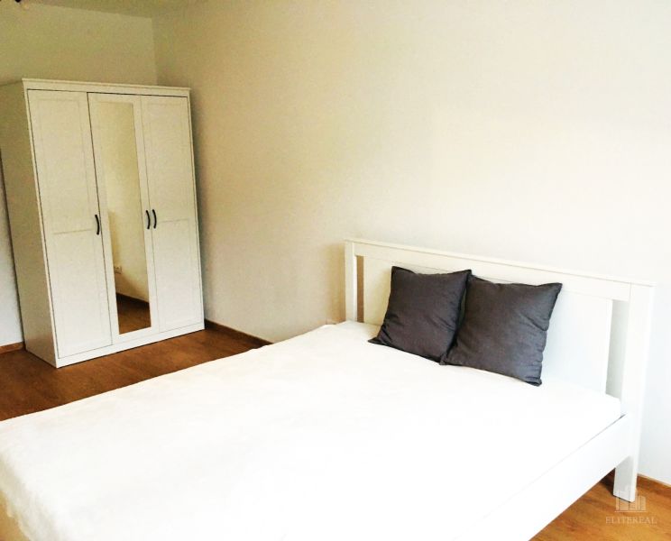 Bedroom in a 2-room apartment with a white bed and wardrobe on a wooden floor.