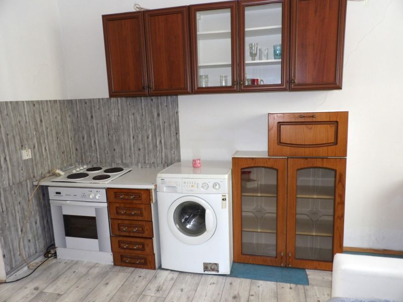 A kitchen in a 2-room apartment with an electric oven, washing machine, and a floor with a wooden decor.