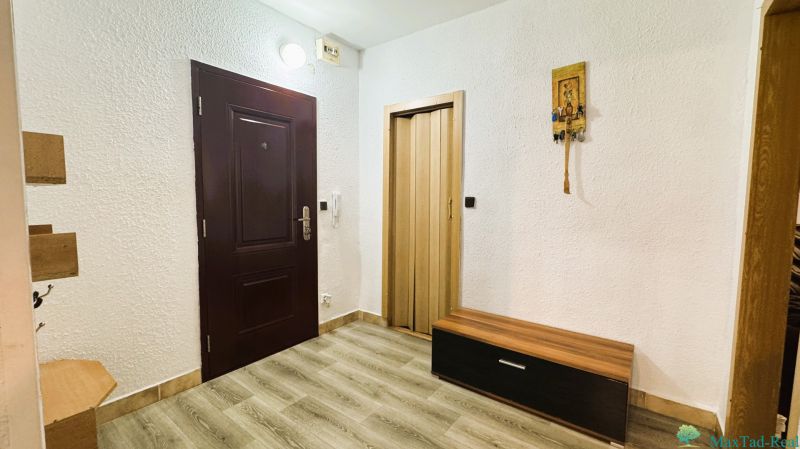Interior of a 4-room apartment with white walls, wood-patterned flooring, and dark doors.