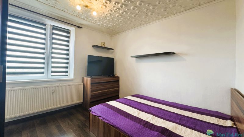 Bedroom in a 4-room apartment with a bed, television, wood-patterned flooring, and modern blinds.