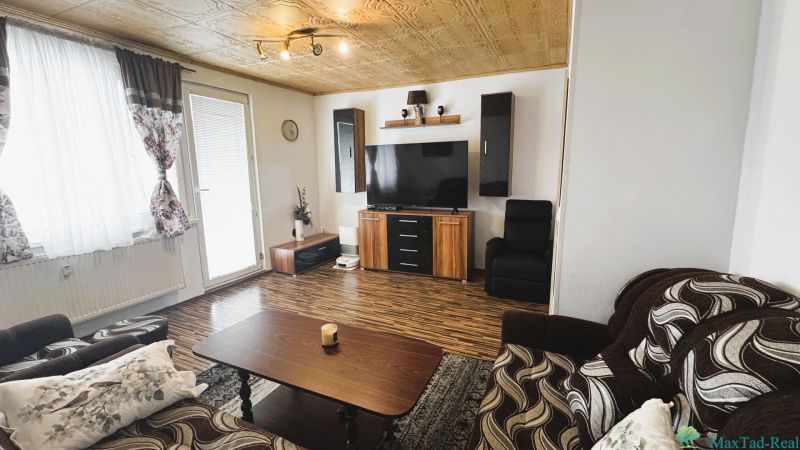 Living room in a 4-room apartment with a wooden decor floor and a TV on the wall.