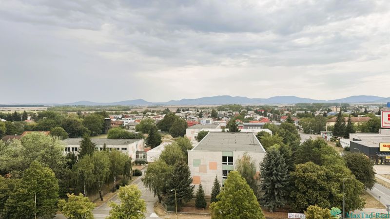 A view of Komenského Street in Trebišov with buildings and greenery.