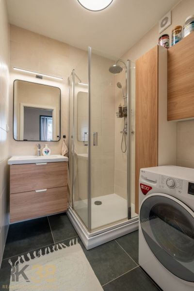Bathroom in a 3-room apartment with a washing machine, shower, and sink with storage space.