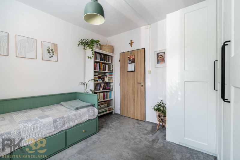 A room in a 3-room apartment with a bed, books, plants, and a lamp.