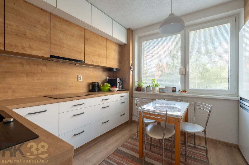 A kitchen with a wooden decor floor in a 3-room apartment, with a dining table by the window.