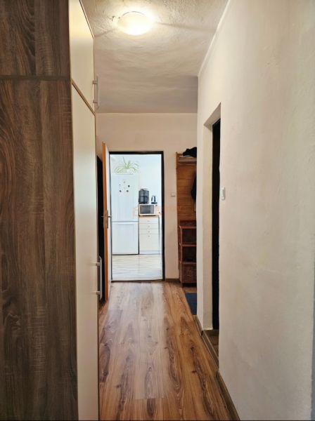 A hallway in a family house with a wooden decor floor and a view into the kitchen.