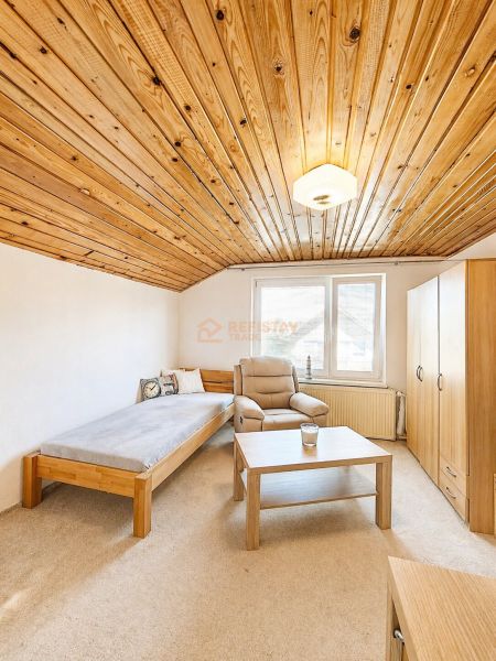 Interior of a family house with a wooden ceiling, an armchair, and a bed next to the window.